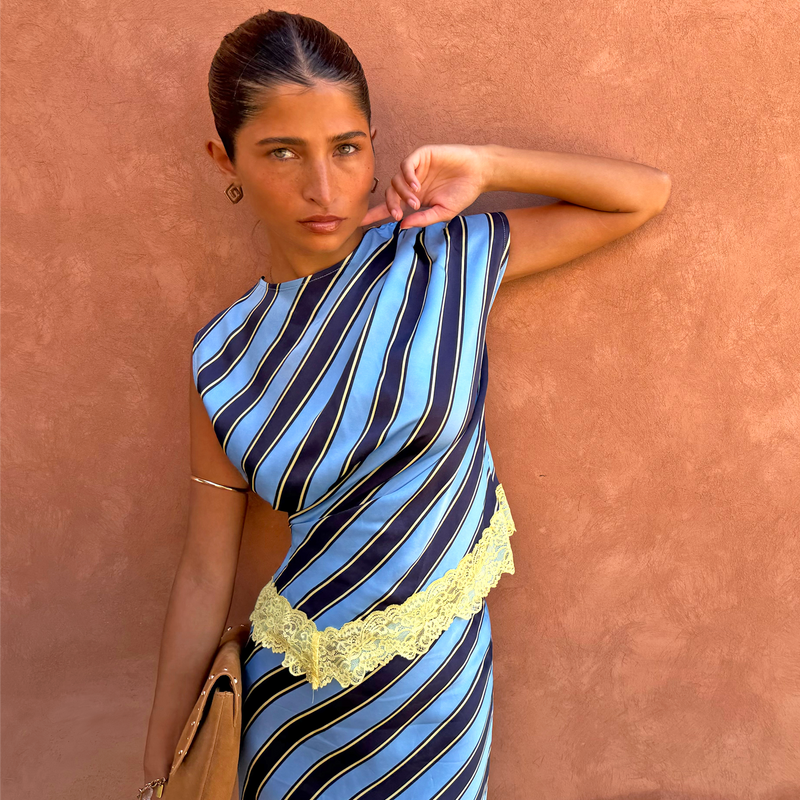 Stripe A-Symmetrical Top in blue diagonal print with yellow lace trim, shown against a terracotta wall.