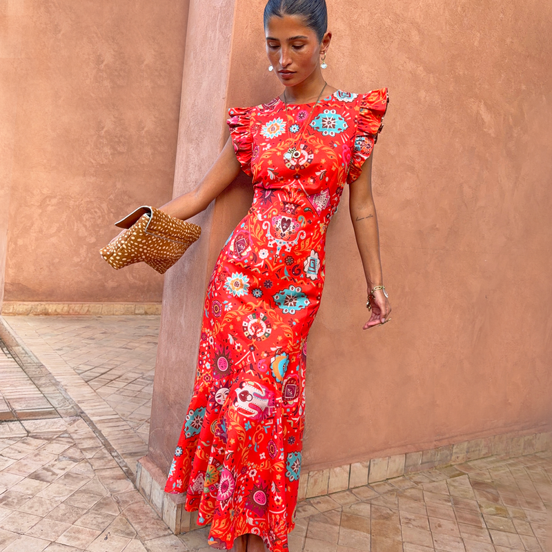 Modella in abito Tomato Tapestry Frida rosso con maniche a volant e stampa con motivi solari.
