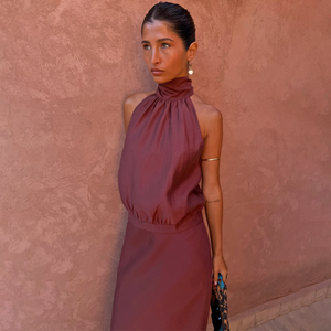 Chocolate Billie Top with a high halterneck and multi-wear scarf detail against a textured terracotta wall.