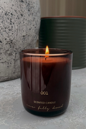 Lit NFD Eau De Parfum Candle 001 in a dark burgundy glass vessel with gold lettering and a flickering flame.