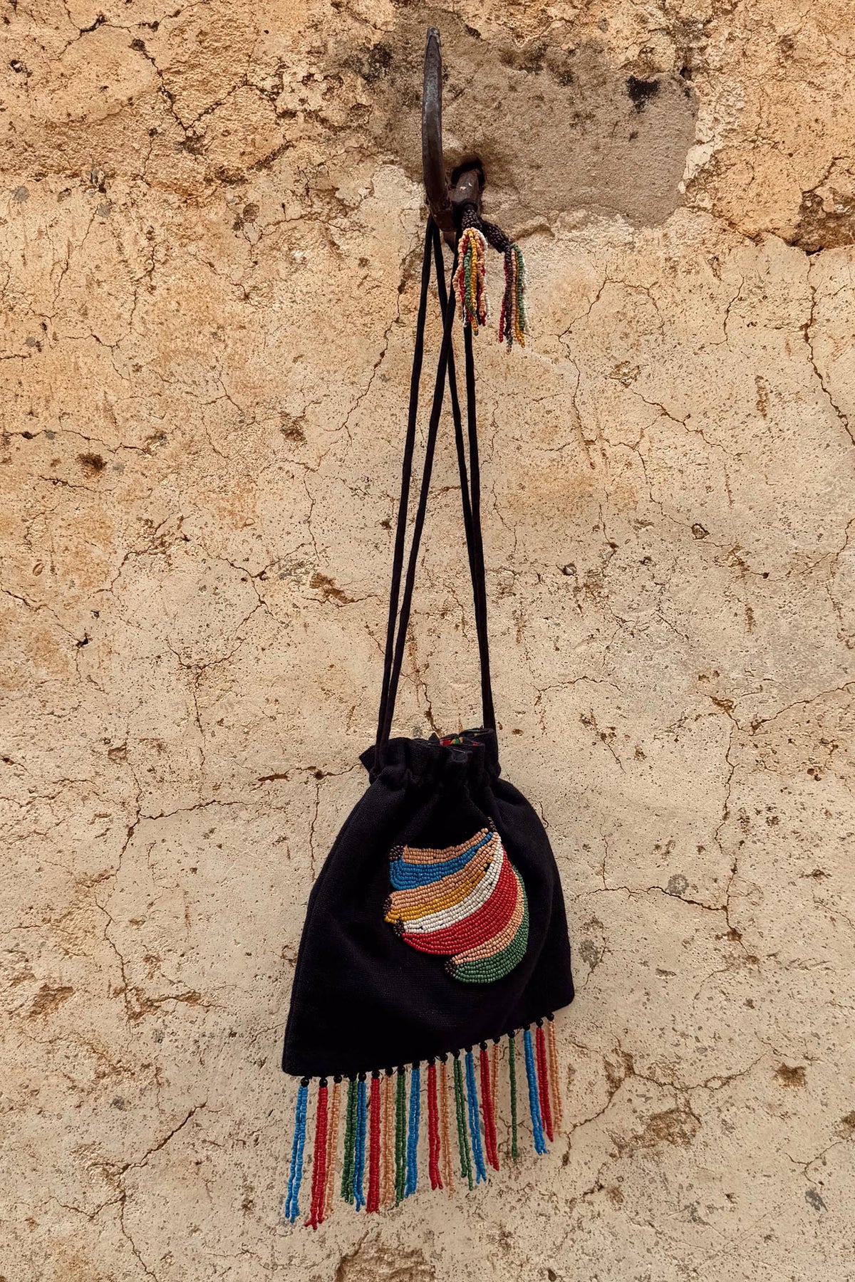 Black Banana Pouch Bag with a colourful beaded banana motif and multicolour fringe hanging on a rustic stone wall.