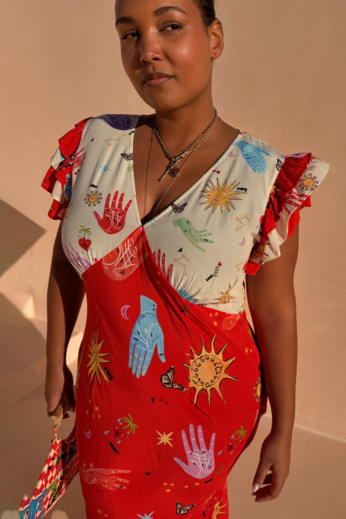 Red Celestial Midi Dress featuring a sun and hand print, V-neck blouson top and ruffled sleeves on a curve model.