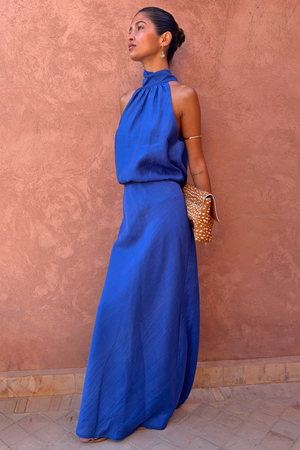 Cobalt Daphne Skirt co-ord with a matching high-neck top and leopard print clutch against a terracotta wall.