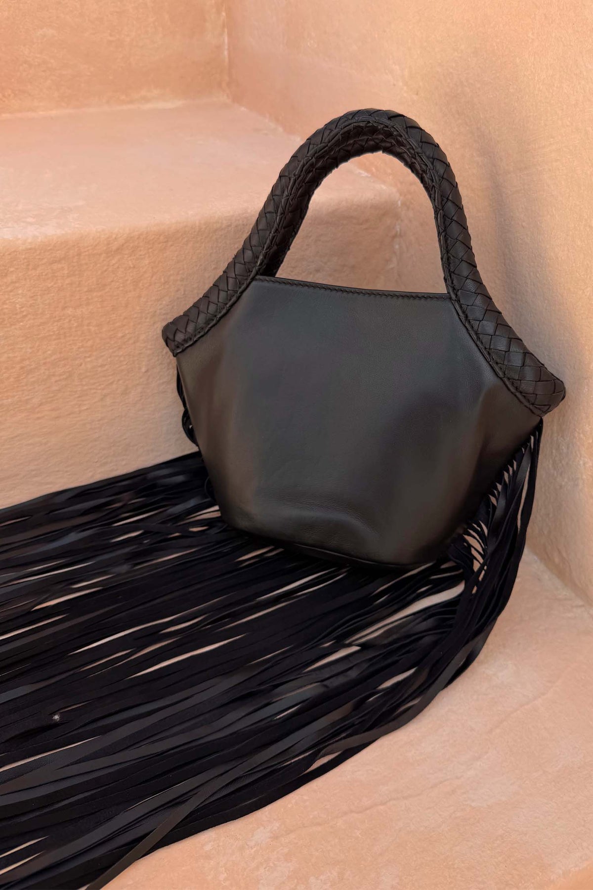 Black Leather Fringe Bag with a plaited handle and fringe detailing, resting on stone steps.