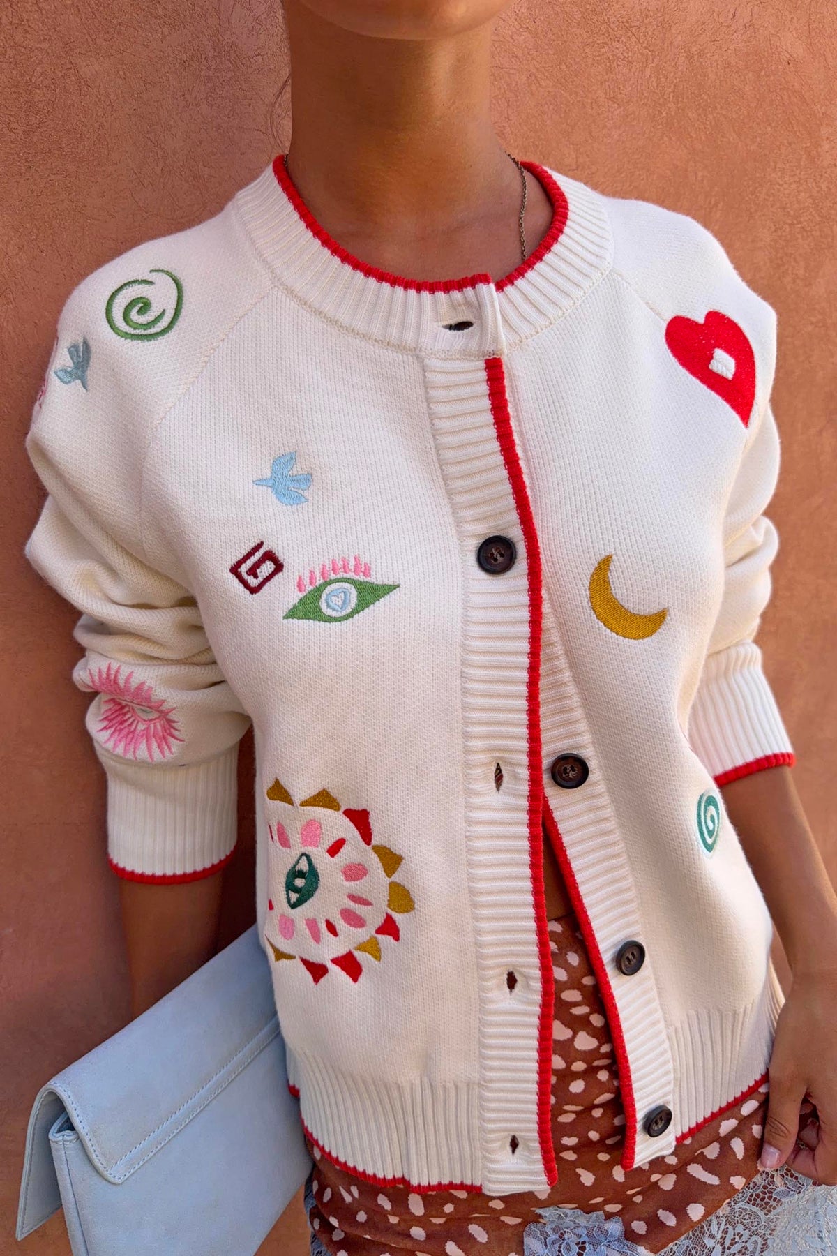 Cardigan Cheryl Morocco Charms panna con ricami colorati, profili rossi e bottoni frontali.