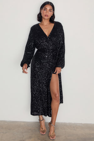 Black Sequin Kira Wrap Dress featuring a multi-wear wrap style, long sleeves, and a leg slit on a model.