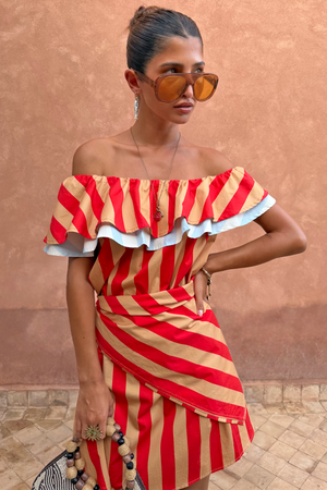 Tomato Stripe Scarf in red and tan styled as a multi-wear ruffled top against a terracotta wall.