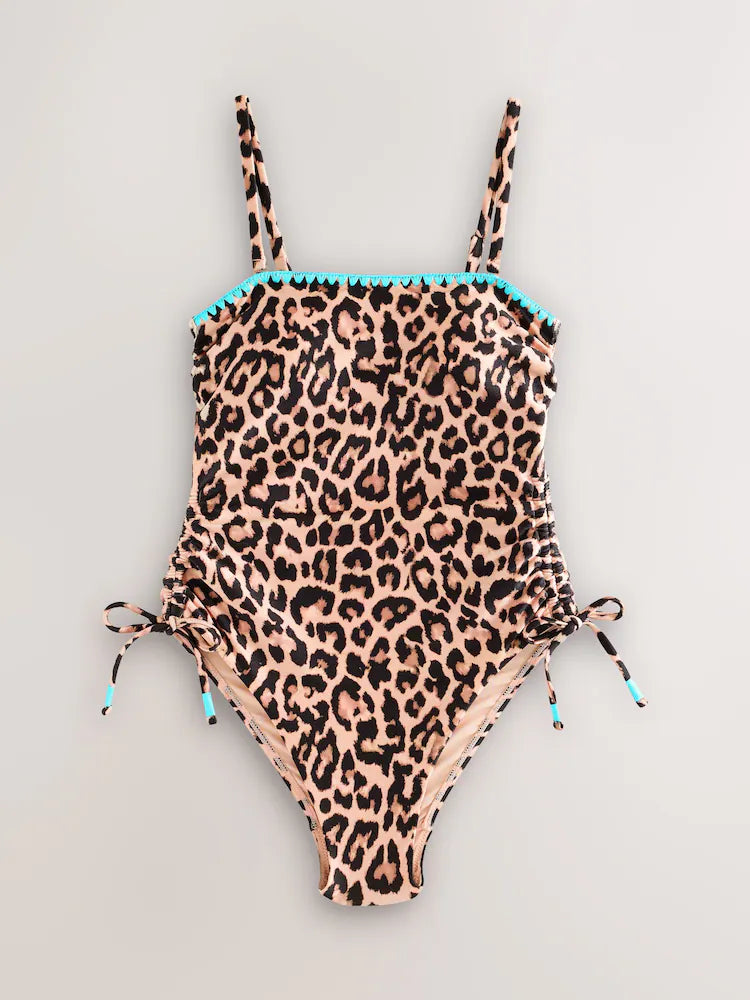 Leopard bandeau swimsuit with blue whipstitch embroidery and ruched side ties, shown in a flat lay.