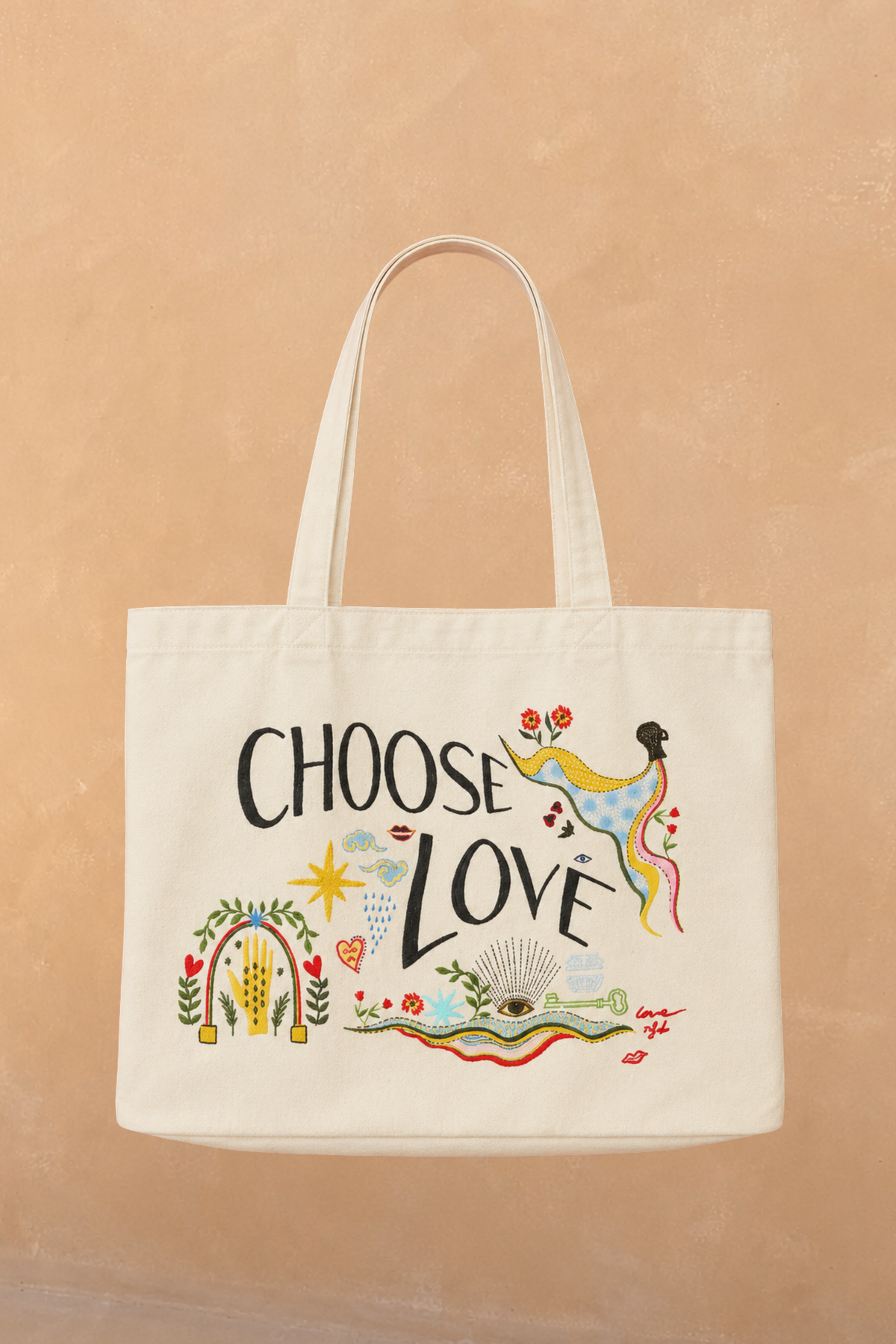 Choose Love Tote Bag in cream recycled cotton featuring colourful graphic artwork and black text against a tan wall.
