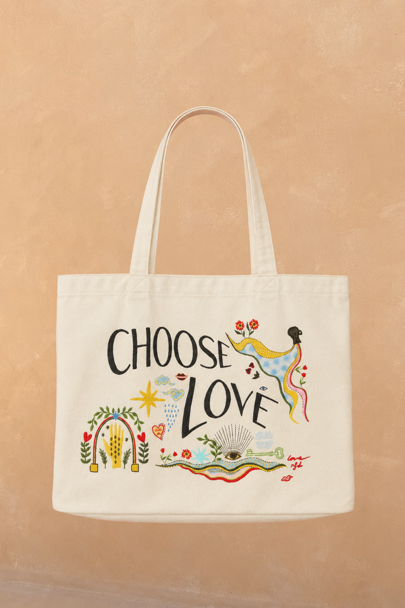Choose Love Tote Bag in cream recycled cotton featuring colourful graphic artwork and black text against a tan wall.