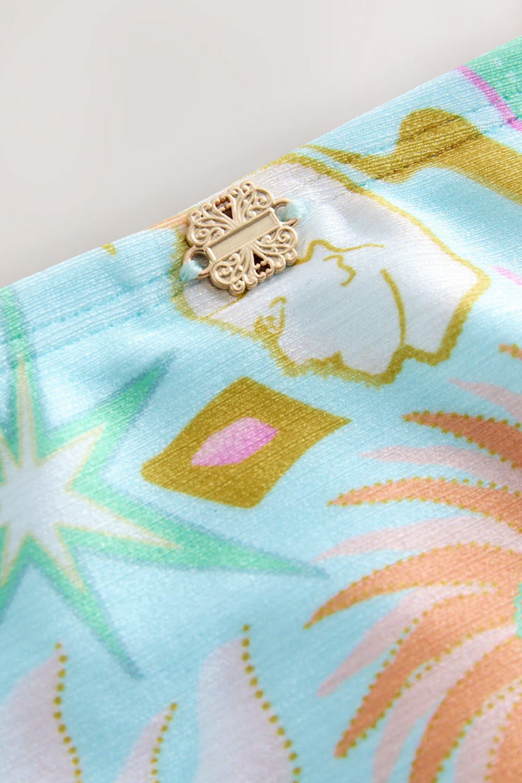 Blue Dreamer High Waist Brief detail with a gold metal NFD logo and sun and palm motifs on blue swim fabric.