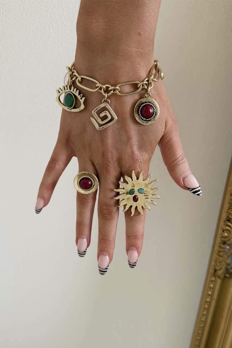 Brushed gold Deloris Charm Bracelet with eye and stone charms, styled on a hand with matching sun and stone rings.
