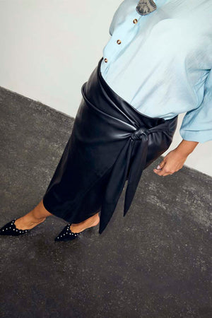 Iconic Black Vegan Leather Wrap Skirt with a tulip shaped tie, styled with a blue shirt and studded black mules.