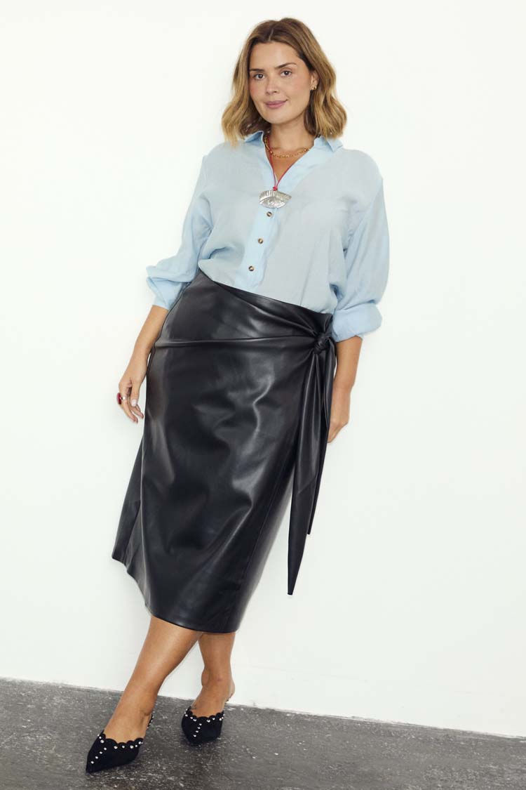Black vegan leather Jaspre wrap skirt with a tulip-shaped tie, styled with a light blue shirt.