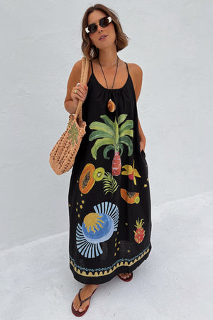Black Rio Maxi Dress with hand-painted tropical fruit motifs and thin straps, styled with a crochet bag and sunglasses.