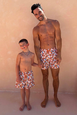 Matching banana print swim shorts in cream with orange drawstrings on a man and boy for a family vacation look.