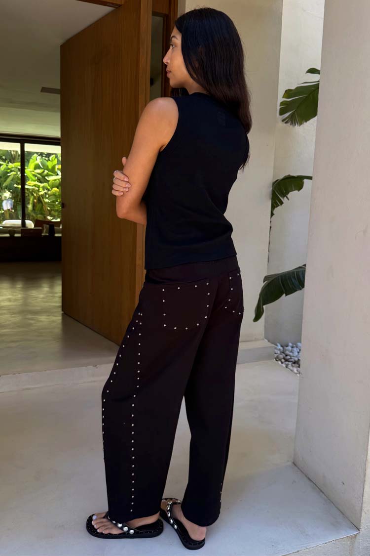 Jeans barrel neri con borchie argentate su tasche e fianchi, indossati di profilo da una modella.