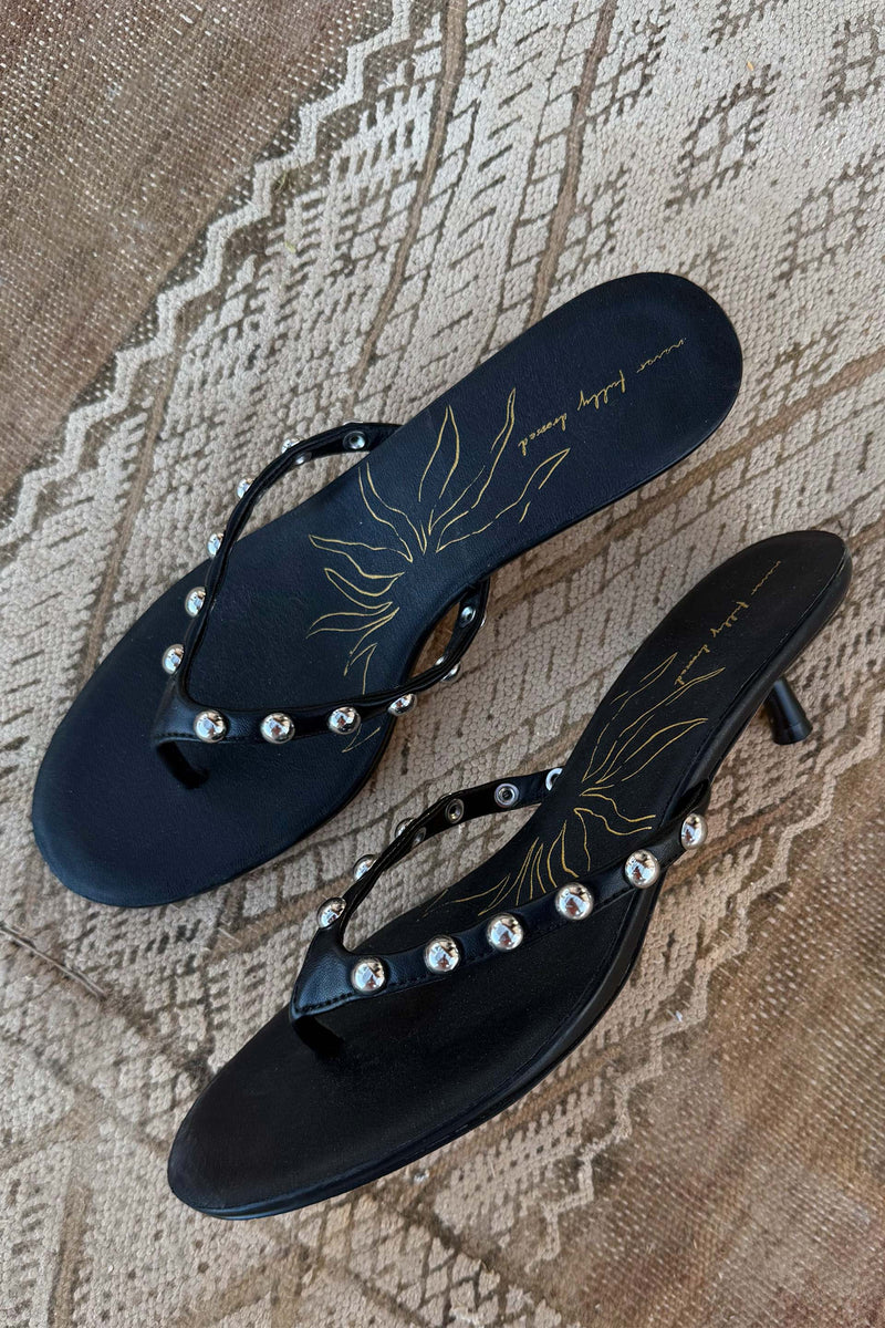 Black Stud Sandal Mules in leather with silver studs, a low kitten heel and signature sun motif on a patterned rug.
