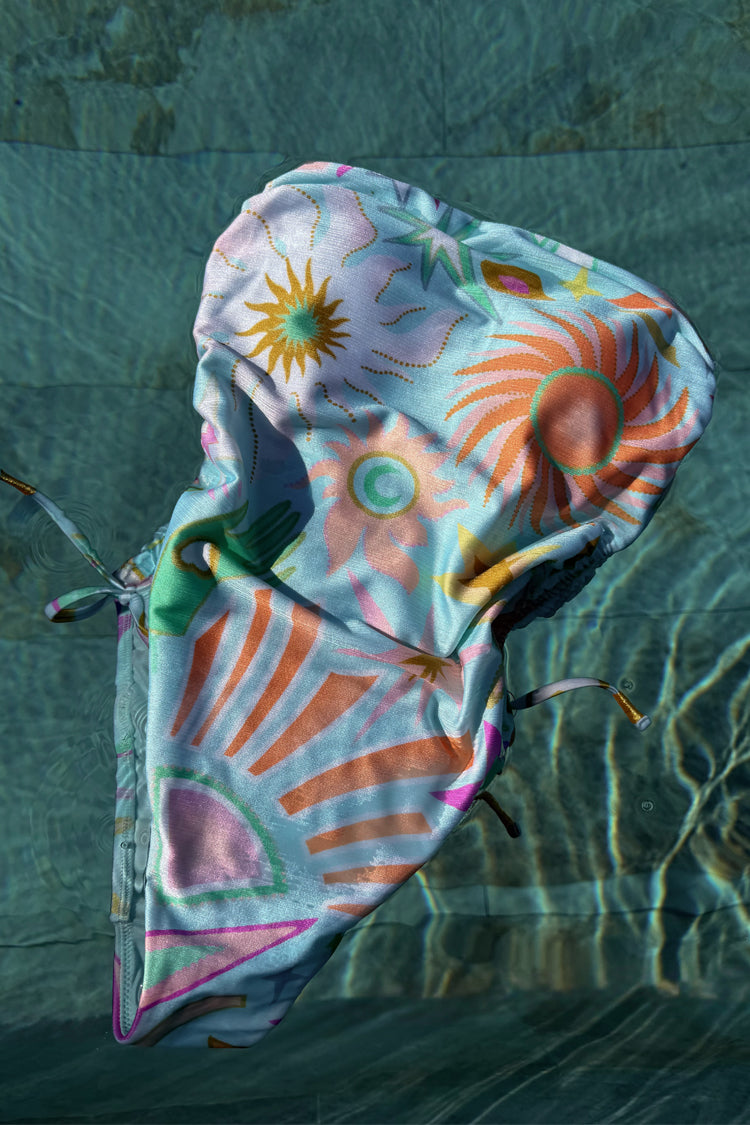 Starburst Bandeau Swimsuit in soft blue with abstract sun and palm prints, floating in pool water.