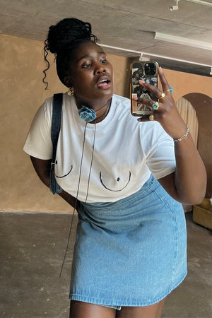 White Boob T-shirt with black line art, styled with a blue denim skirt in a mirror selfie.