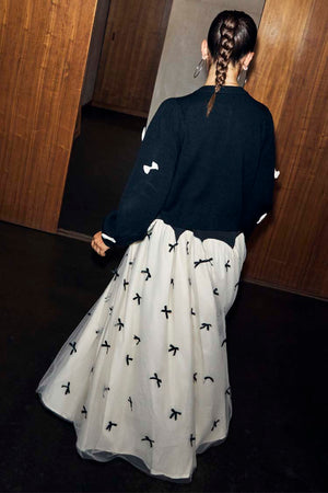 Black Bow Sophie Cardigan with 3D cream bows, shown from the back with a tie-neck detail and bow-print maxi skirt.
