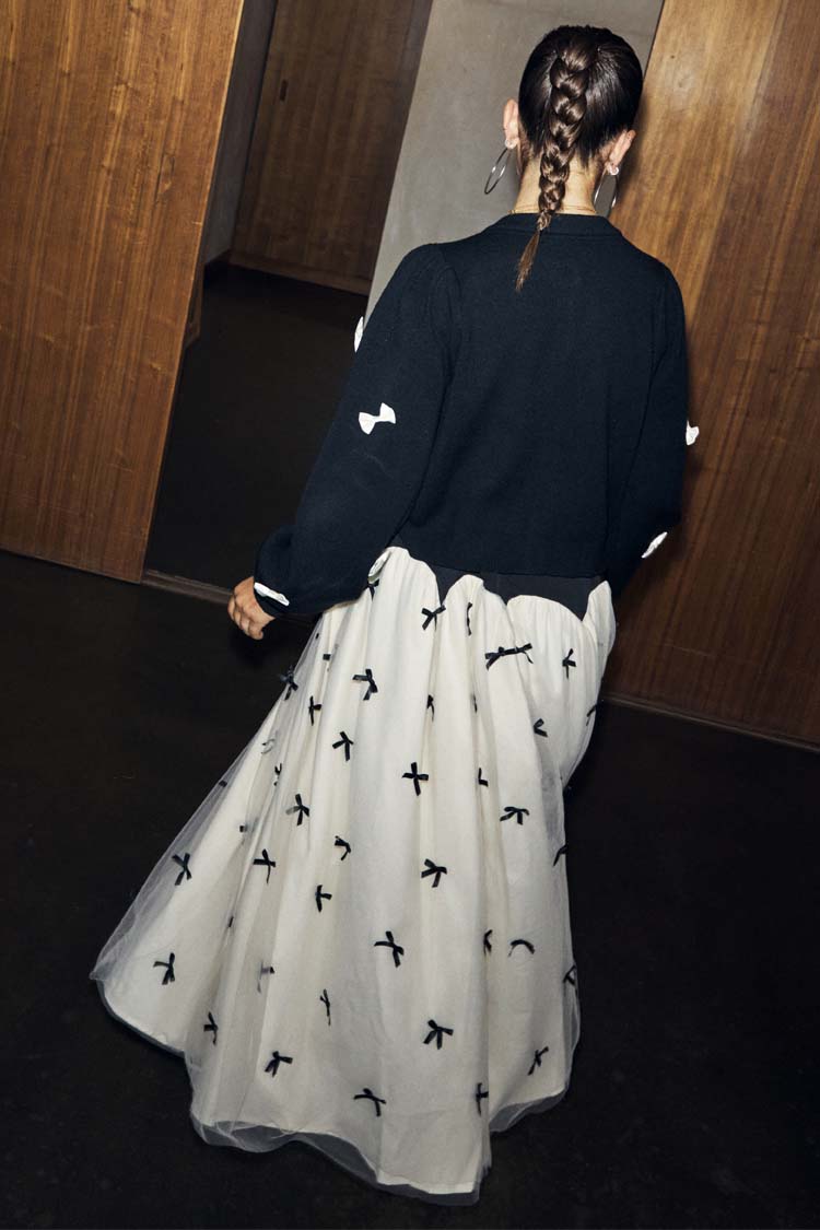 Black Bow Sophie Cardigan with 3D cream bows, shown from the back with a tie-neck detail and bow-print maxi skirt.