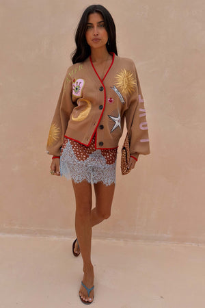 Camel Mystical Cardigan with celestial embroidery and red trim worn over a patterned blue lace dress.