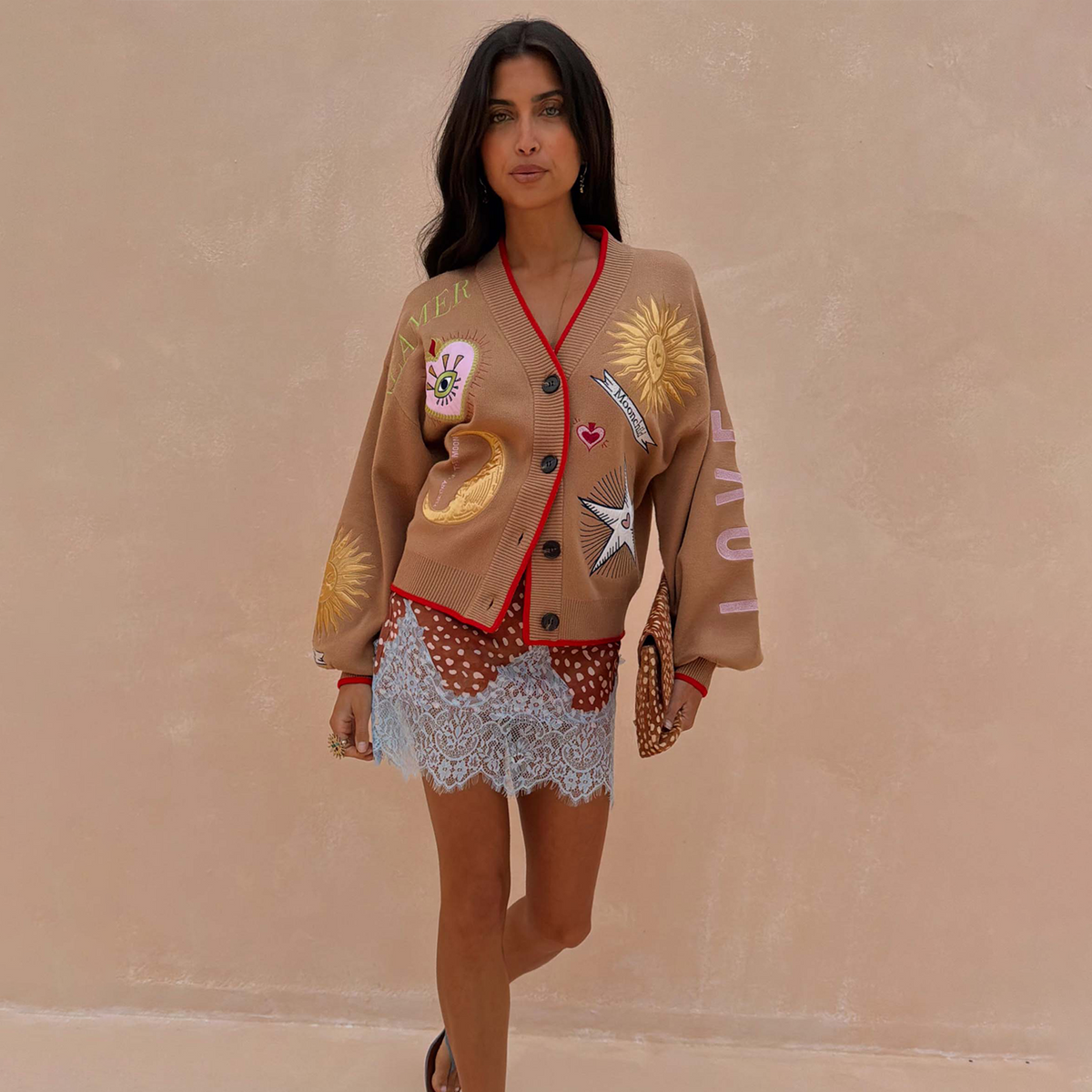 Cardigan Camel Mystical con ricami di sole e luna e profili rossi, indossato da una modella su sfondo neutro.