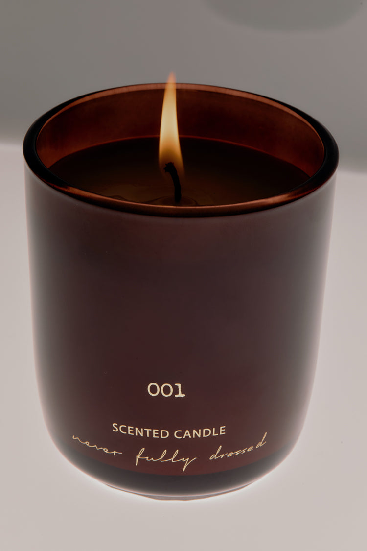 NFD Eau De Parfum Candle 001 in a burgundy glass jar with a lit wick and gold script logo.