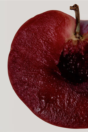 Deep red sliced plum with a dark stone, highlighting a key fragrance note for the NFD Candle 001.