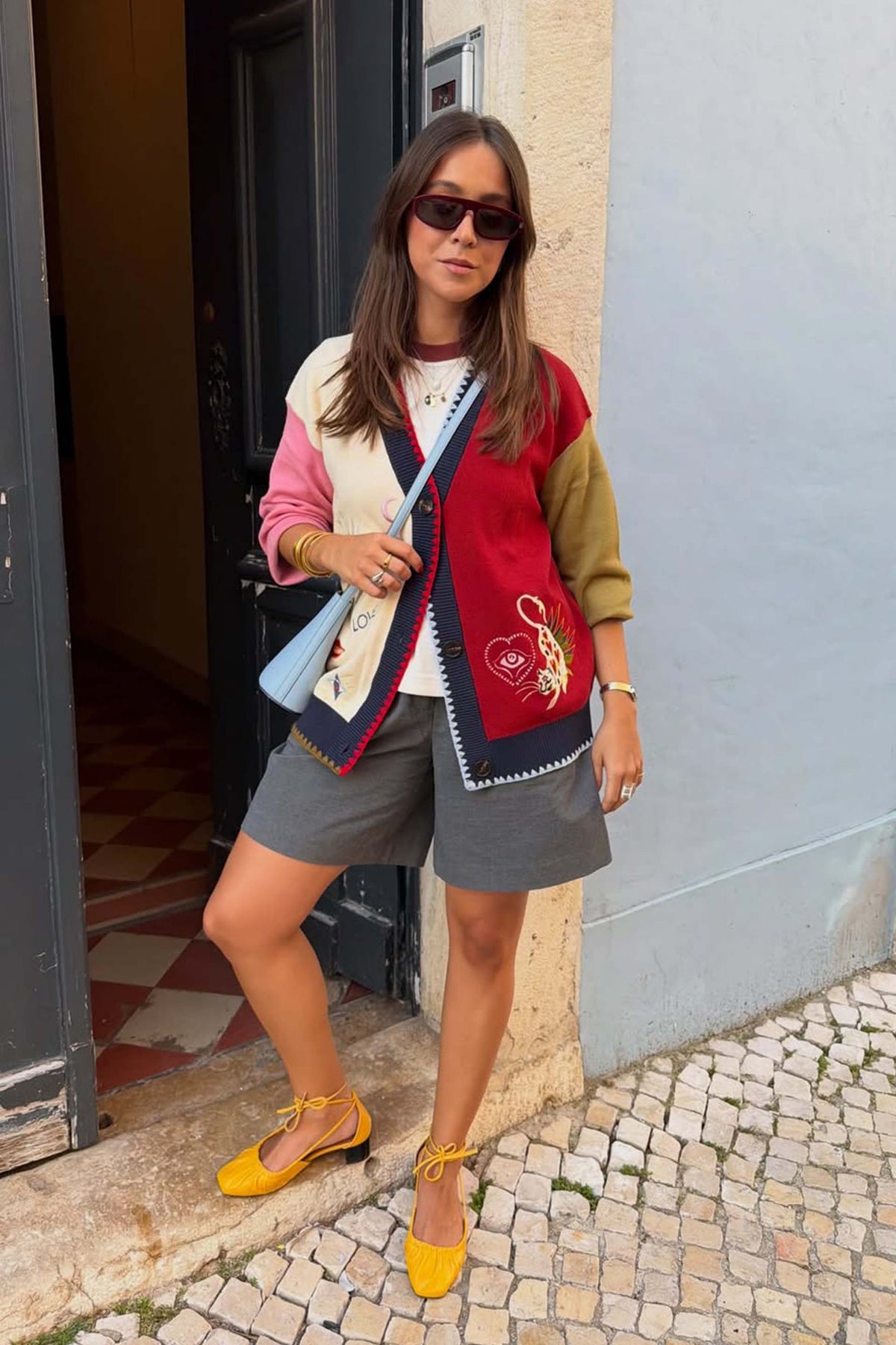 Cardigan Mystical Martha color-block in maglia con ricami, pantaloncini grigi e scarpe gialle.