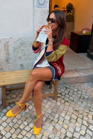 Cardigan Mystical Martha color-block con ricami, indossato con scarpe gialle su una panchina.