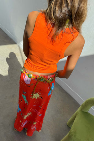 Red satin Celestial Dorris Skirt with hand-painted motifs, styled with an orange tank top and a statement belt.