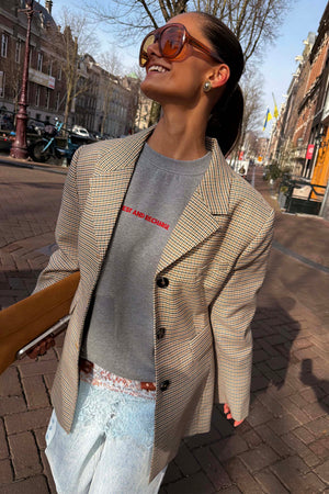 Blazer a quadri marrone e beige con felpa grigia e occhiali da sole in un look street style all'aperto.