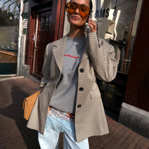 Blazer a quadri marrone indossato con felpa grigia e jeans in un look street style urbano.