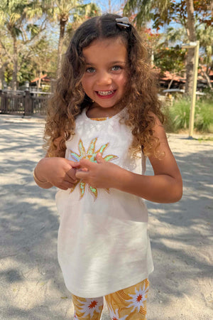 Girl’s Yellow Sun Cotton Set featuring a cream sequinned sun vest and yellow soleil motif trousers in a vacation setting.