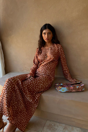 Fawn Soho Dress in brown satin-esque deer print with long sleeves, shown on a seated model with a printed clutch.