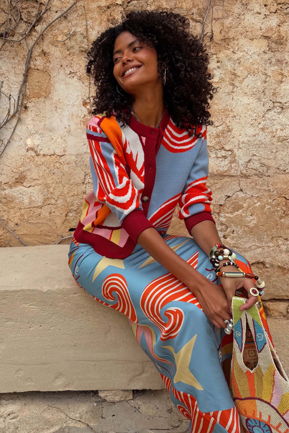 Cardigan Hollie Dolce Vita a stampa vivace azzurra e rossa, indossato da una modella seduta all'aperto.