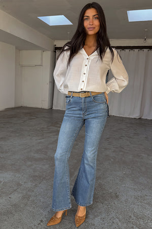Jeans Scallop in denim blu dalla silhouette a zampa anni '70, abbinati a una camicetta bianca.