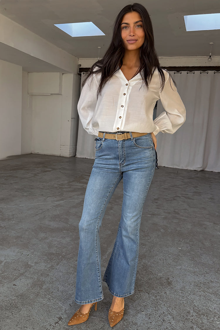 Jeans Scallop in denim blu dalla silhouette a zampa anni '70, abbinati a una camicetta bianca.