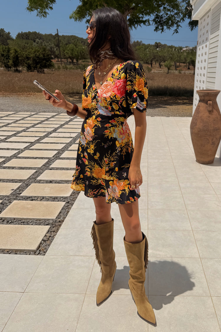 Black Sofia Mini Tea Dress with an orange and pink floral print and frill hem, styled with tan fringe boots.