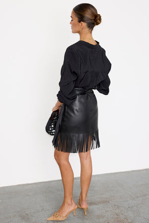 Black Vegan Leather Mini Fringe Jaspre Skirt featuring a wrap tie waist and fringe hem, shown on a model.