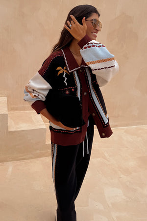 Geometric Knit Cardigan with iconic palm motifs in autumnal tones, styled with matching black joggers.