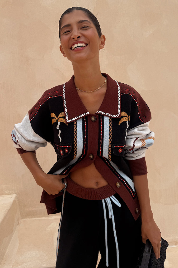 Geometric Knit Cardigan in autumnal tones with palm motif embroidery and a white blanket stitch collar on a smiling model.