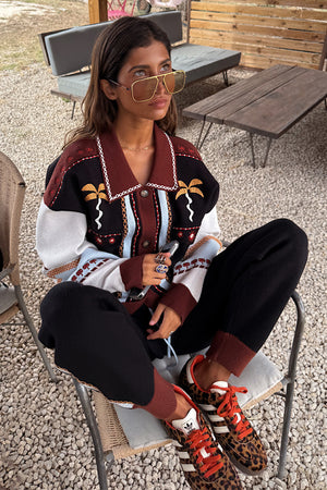 Geometric Knit Cardigan with embroidered palm motifs and autumnal tones, worn by a 5ft4” model in size M sitting outdoors.