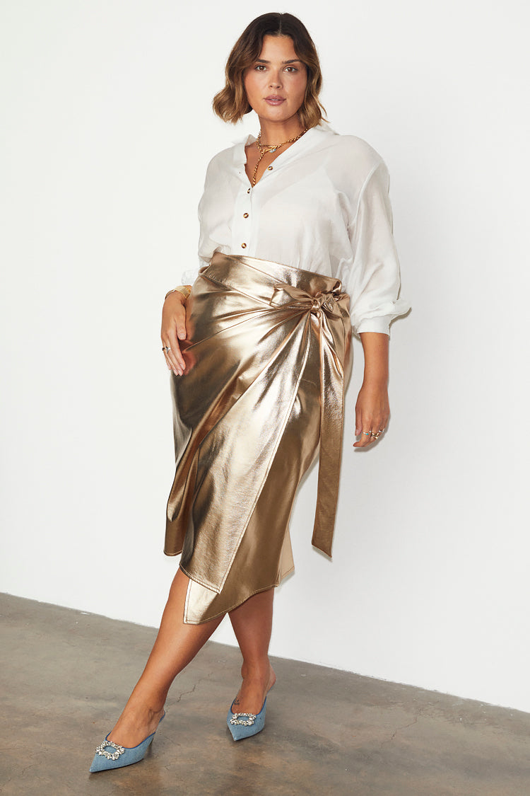 Gold vegan leather Jaspre wrap skirt styled with a white button-down shirt and blue heels.