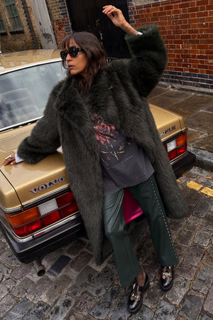 Green Faux Fur Coat in a relaxed fit, leaning against a vintage gold car on a cobblestone London street.