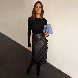Black Vegan Leather Ruffle Jaspre Skirt with side ruffle detailing, styled with a long-sleeve top and blue clutch.