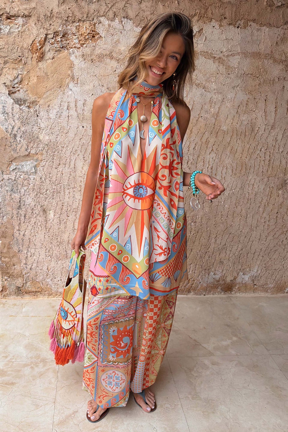 Dolce Vita Josie Mini Dress in sunset tones with an eye motif and halterneck scarf tie, styled for vacation.