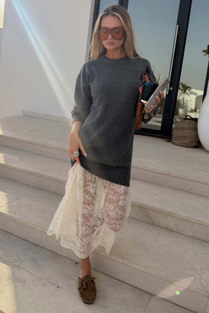 Grey Knit Jumper Dress with a sheer white lace skirt, styled with sunglasses and loafers on stone steps.